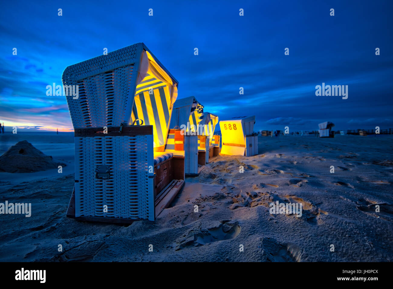 Twilight at the beach of Sank Peter Ording in north Germany. Beach chairs are gentle illuminated by lights during stormy sun set Stock Photo