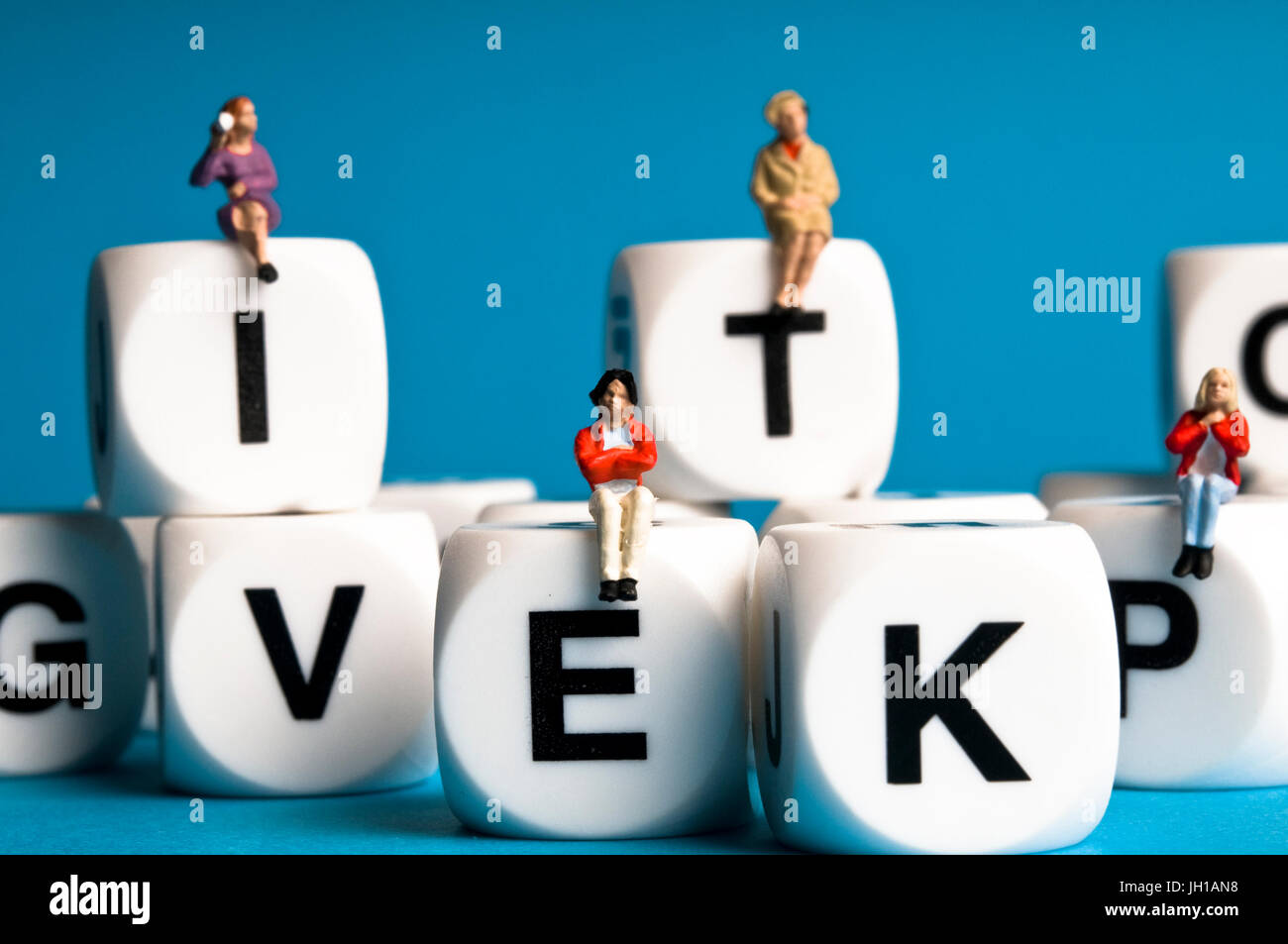 miniature figurines of people sitting on dice with letters, communication, education, socializing concept Stock Photo