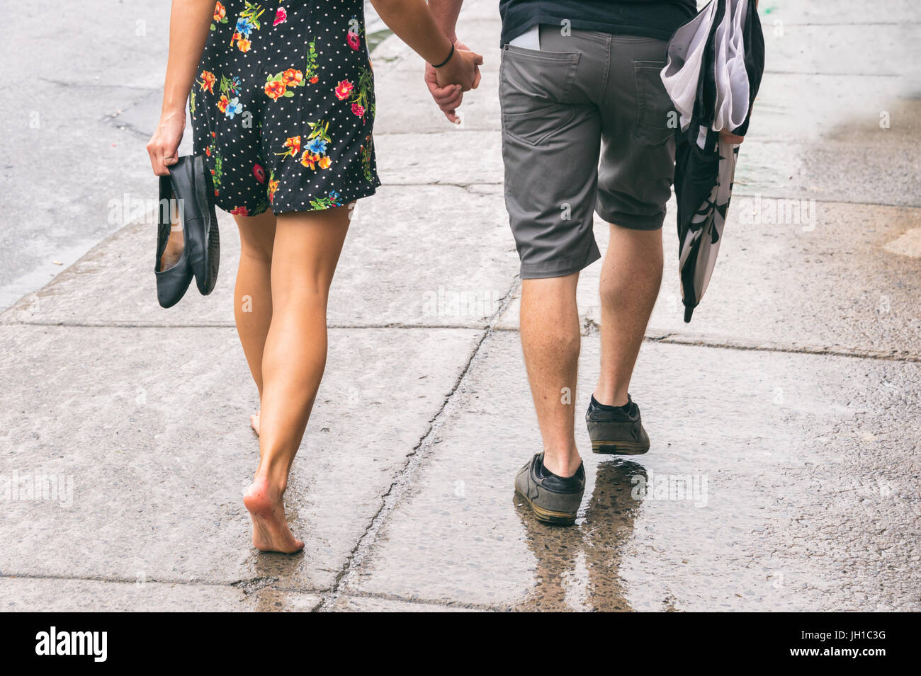Couple on the street under the rain, woman walking barefoot Stock Photo