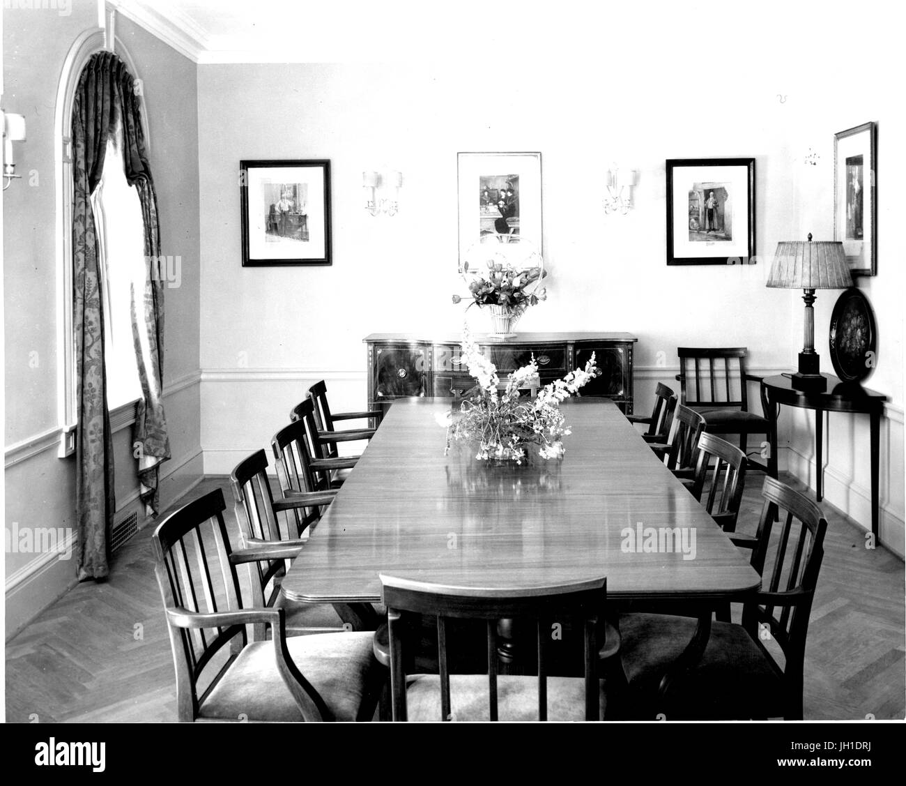 Dining room of the Johns Hopkins Club, featuring a large table, chairs, a cabinet, framed photographs, and sconces, in Baltimore, Maryland, 1930. Stock Photo