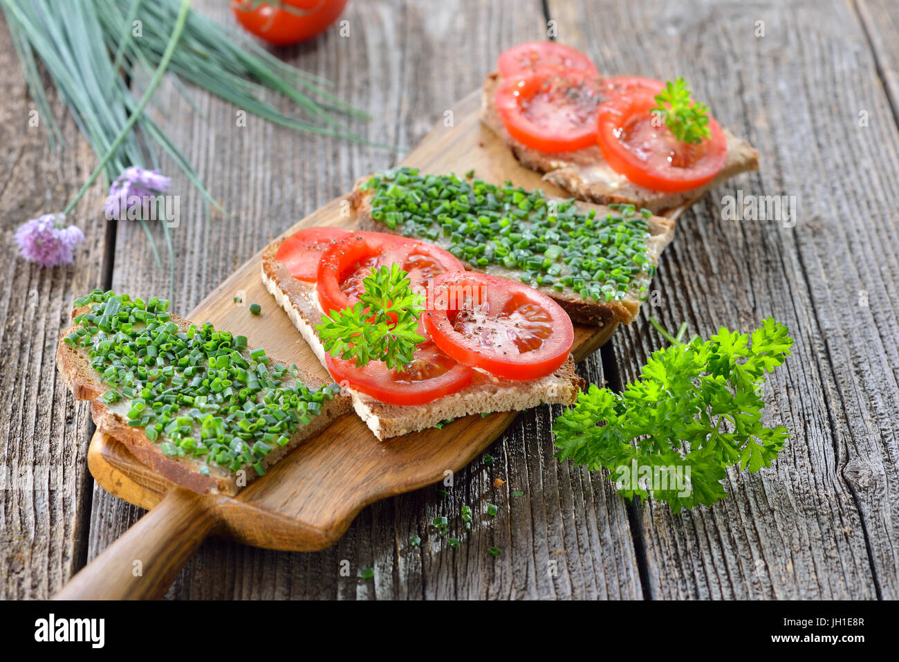Vegetarian snack: Slices of buttered farmhouse bread with fresh chives and tomatoes on a wooden board Stock Photo