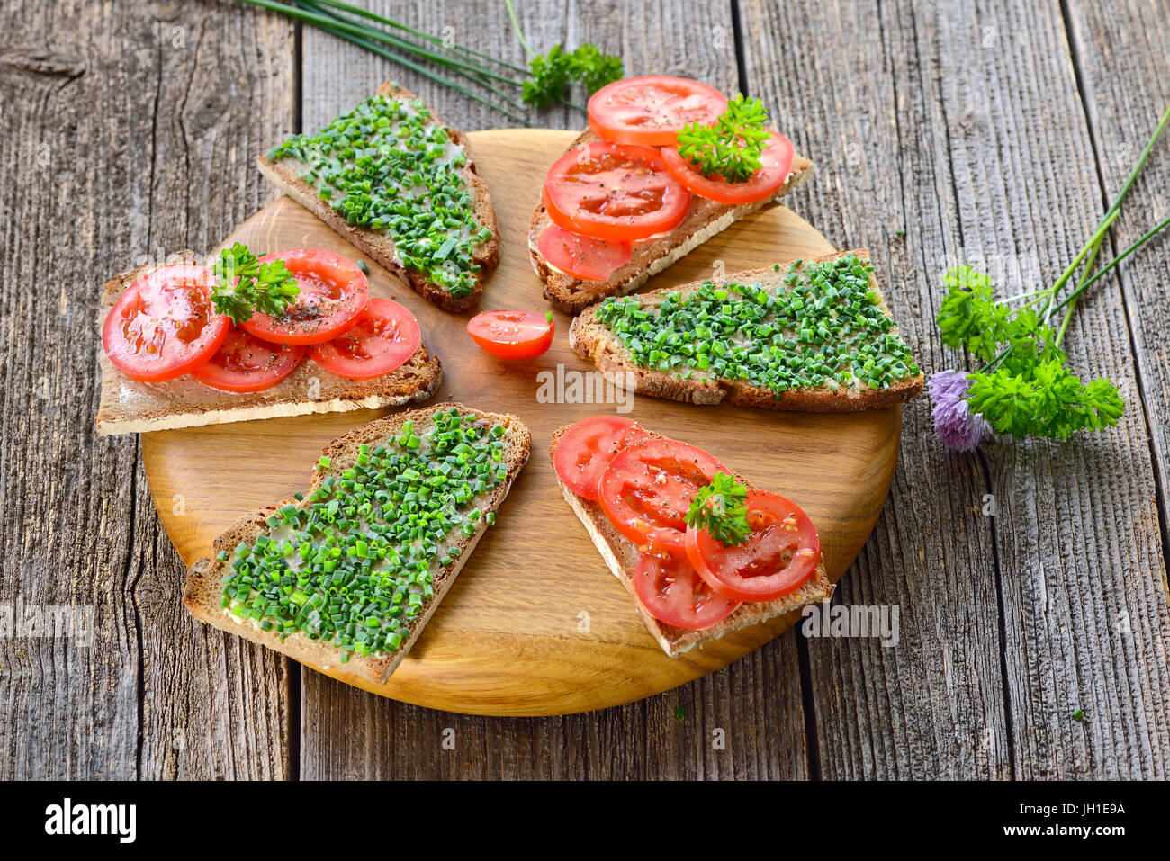 Vegetarian snack: Slices of buttered farmhouse bread with fresh chives and tomatoes on a wooden board Stock Photo