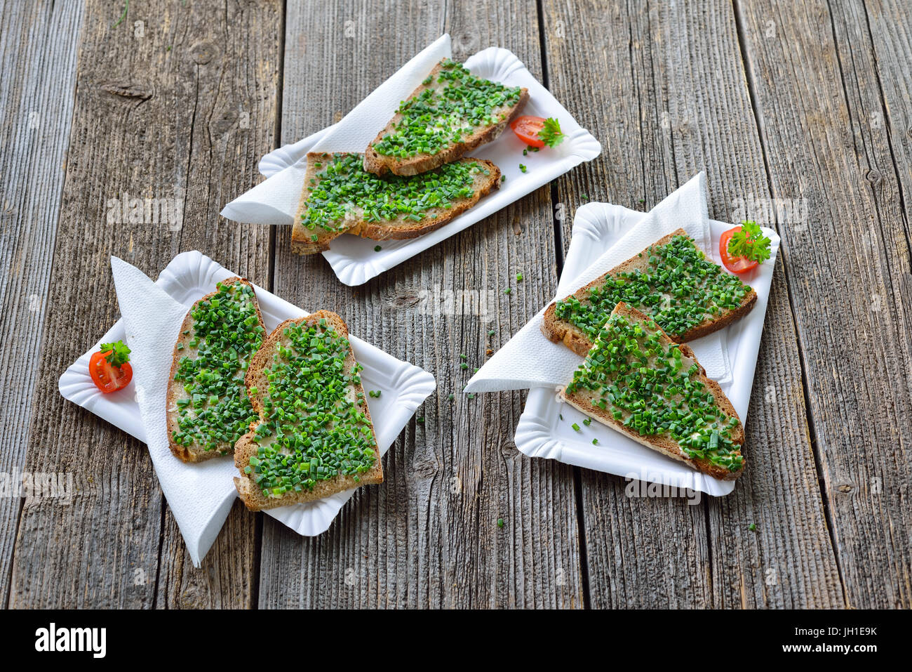 Street food: Slices of fresh farmhouse bread with butter and chopped chives on white paper plates with napkins Stock Photo