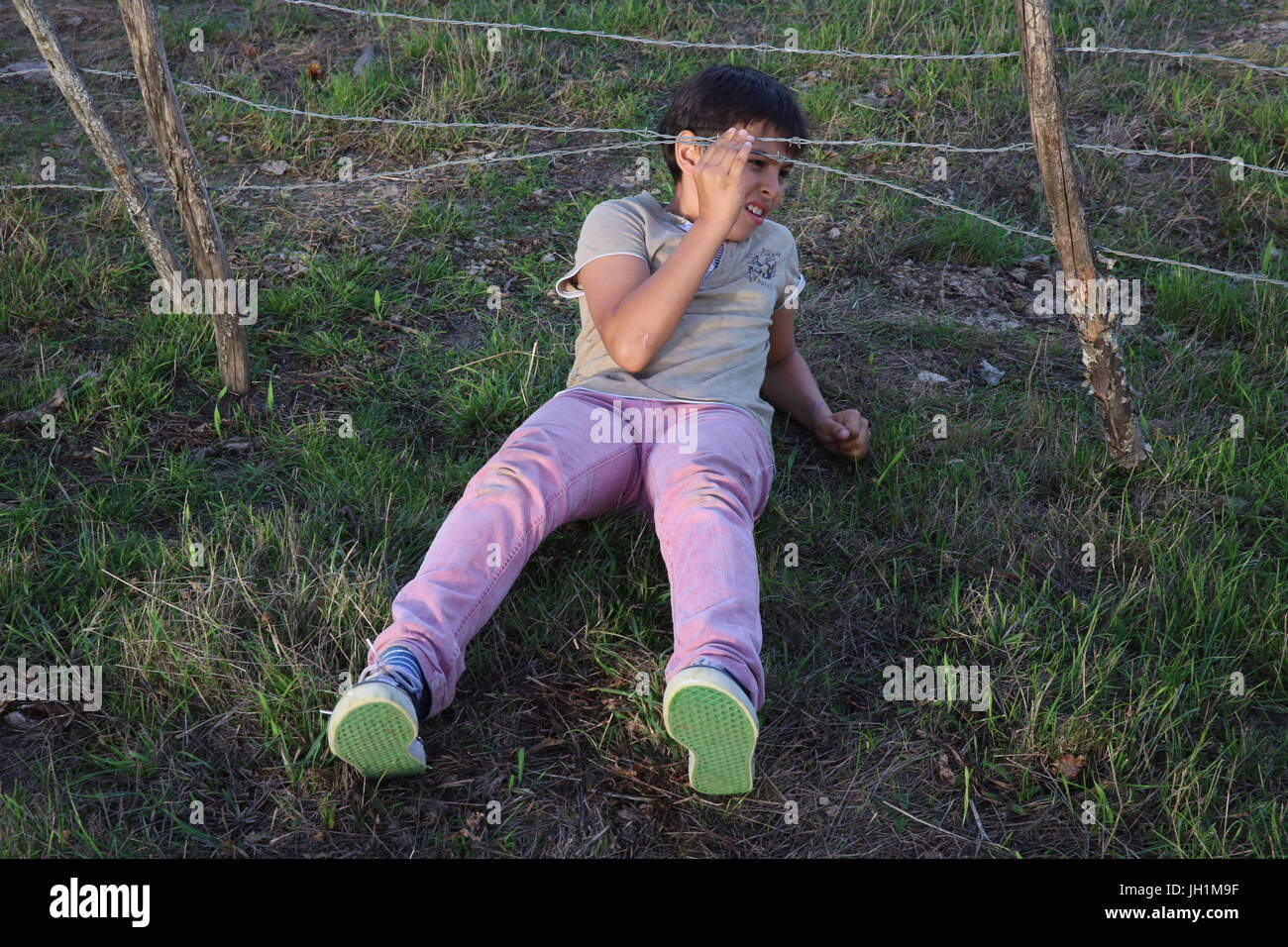 10-year-old boy sliding under a brabed wire fence. France. Stock Photo