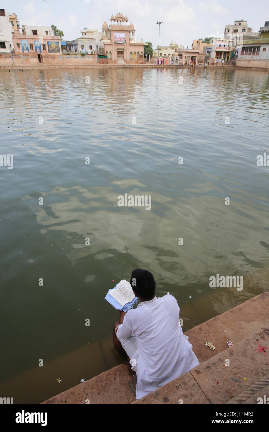 Hindu reading a spiritual book on the steps leading to Goverdan Radha Kund. India. Stock Photo