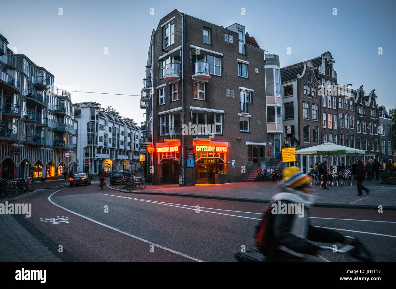 Amsterdam, Netherlands - 25 April, 2017: Adult rides a bicycle in historical part of Amsterdam with typical traditional houses against The Coffeeshop  Stock Photo