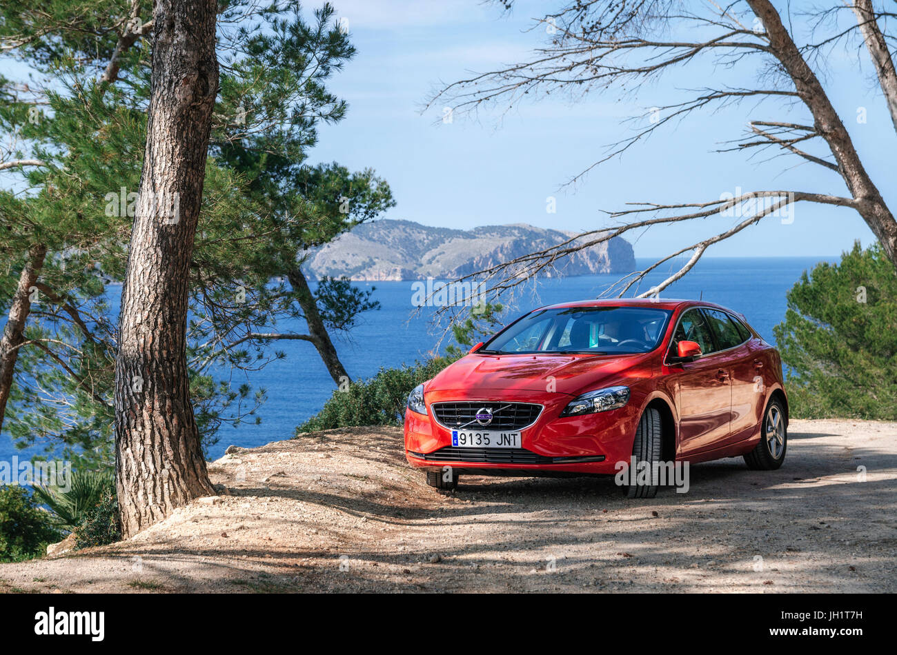 Alcudia, Mallorca, Spain - May 23, 2016: Seascape of Mediterranean Sea with a red car Volvo V40 traveling on the mountain serpentine through the pine  Stock Photo