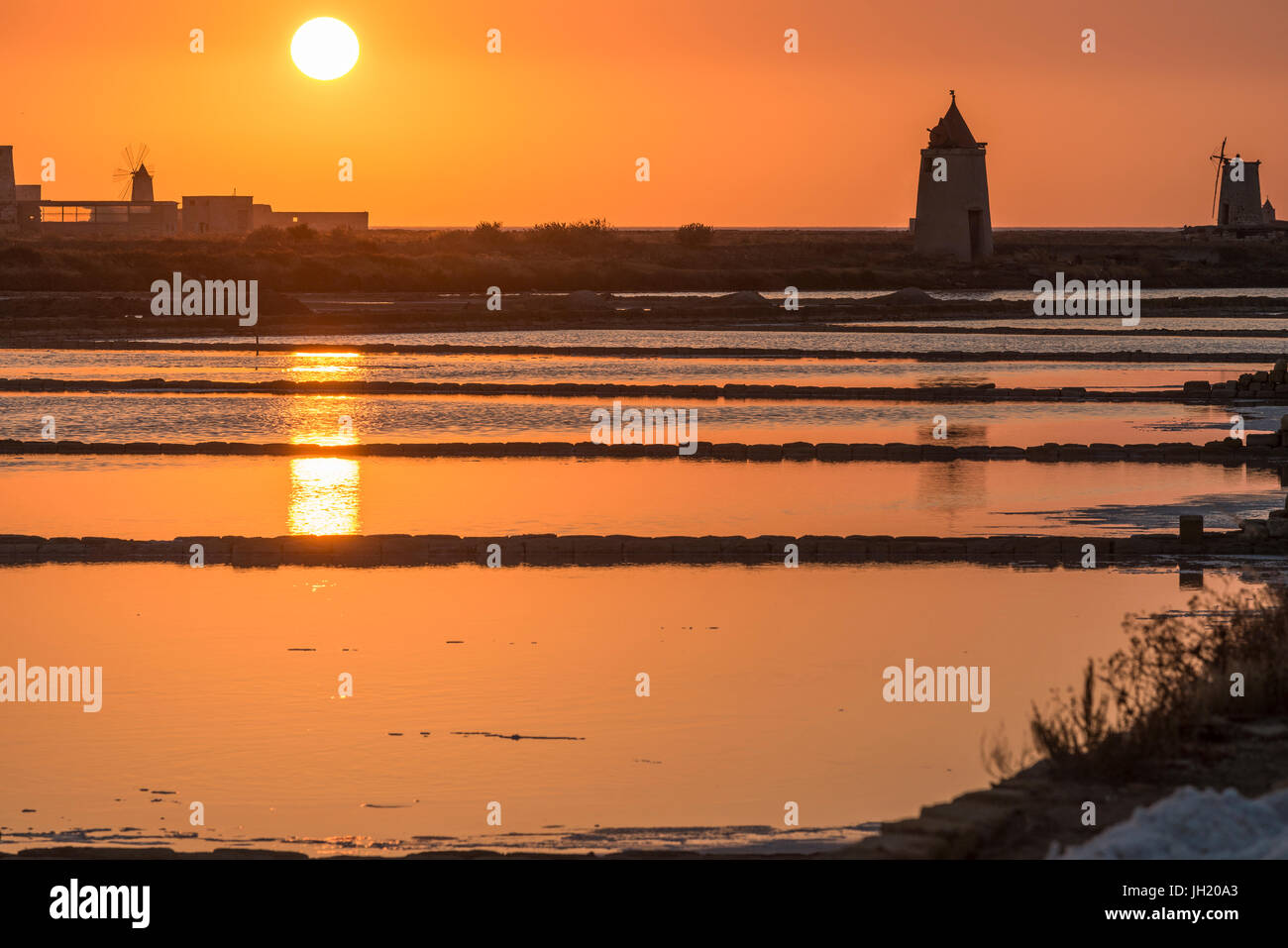 Sunset across the  saltpans and windmills at the wildlife  Reserve near Nubia, south of  Trapani, on the west coast of Sicily, Italy. Stock Photo