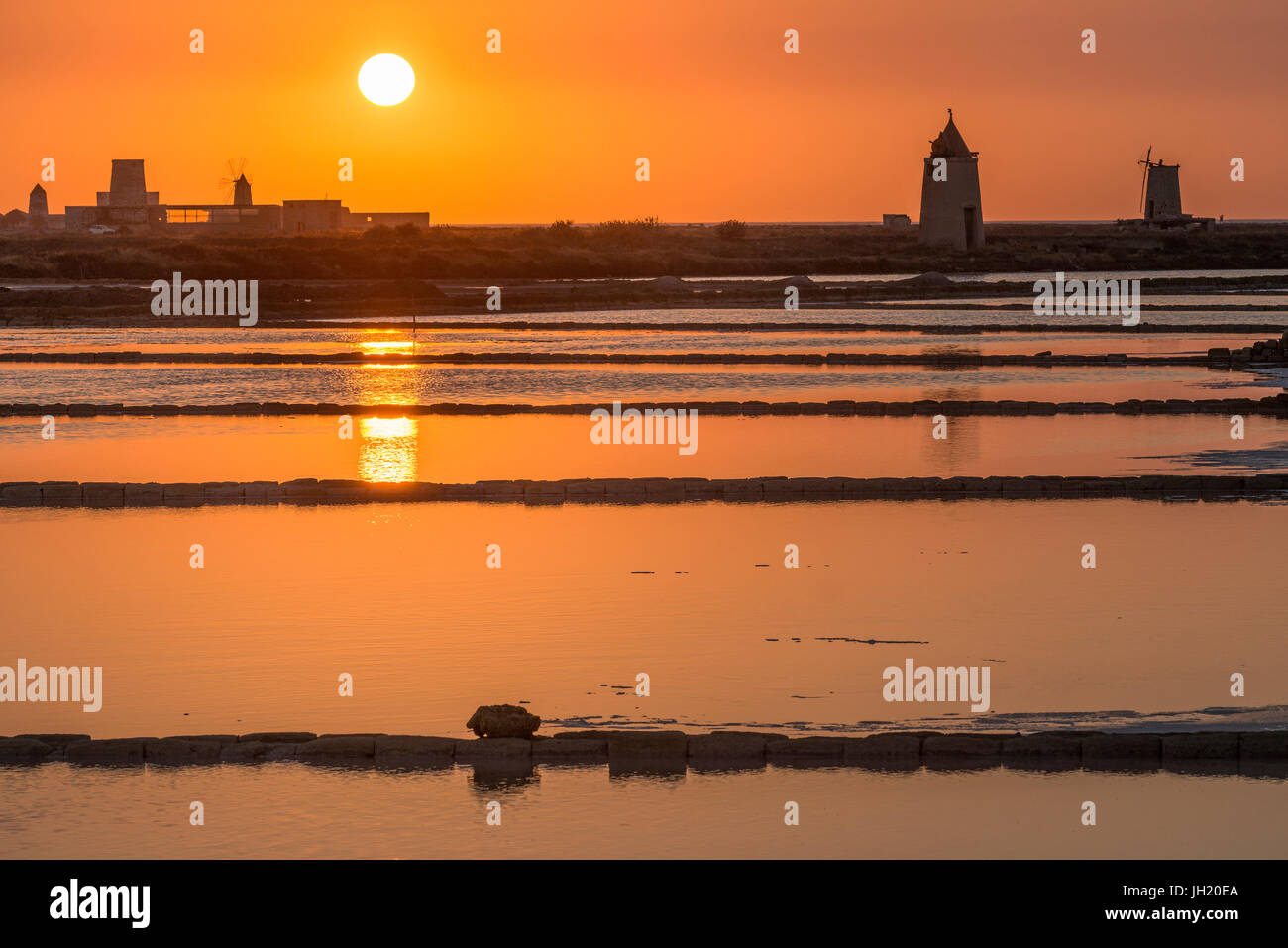 Sunset across the  saltpans and windmills at the wildlife  Reserve near Nubia, south of  Trapani, on the west coast of Sicily, Italy. Stock Photo