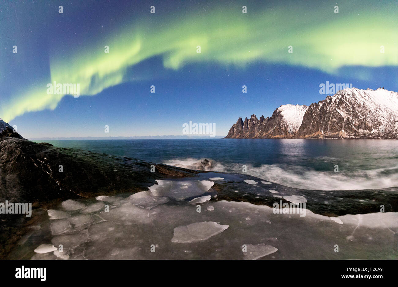 Panorama of frozen sea and rocky peaks illuminated by the Northern Lights, Tungeneset, Senja, Troms, Norway Stock Photo