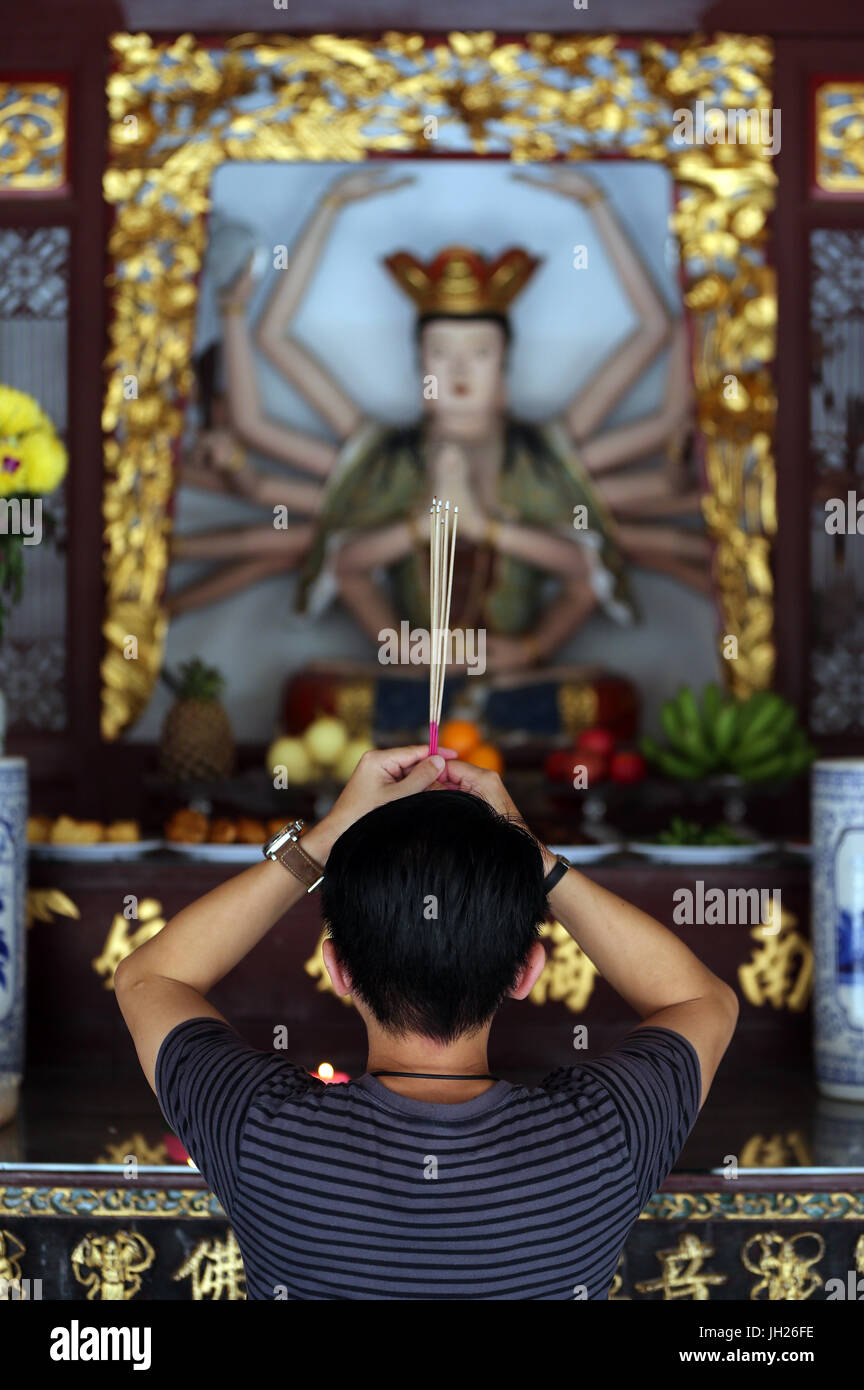 Thian Hock Keng Temple.  A Chinese young man praying and offering incense.  Buddhist Worshipper. Burning incense sticks.  Man praying.  Singapore. Stock Photo