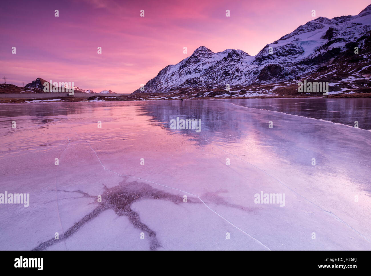 Pink sky at sunset on the frozen Lej Nair framed by snowy peaks, Bernina Pass, Canton of Graubunden, Engadine, Switzerland Stock Photo