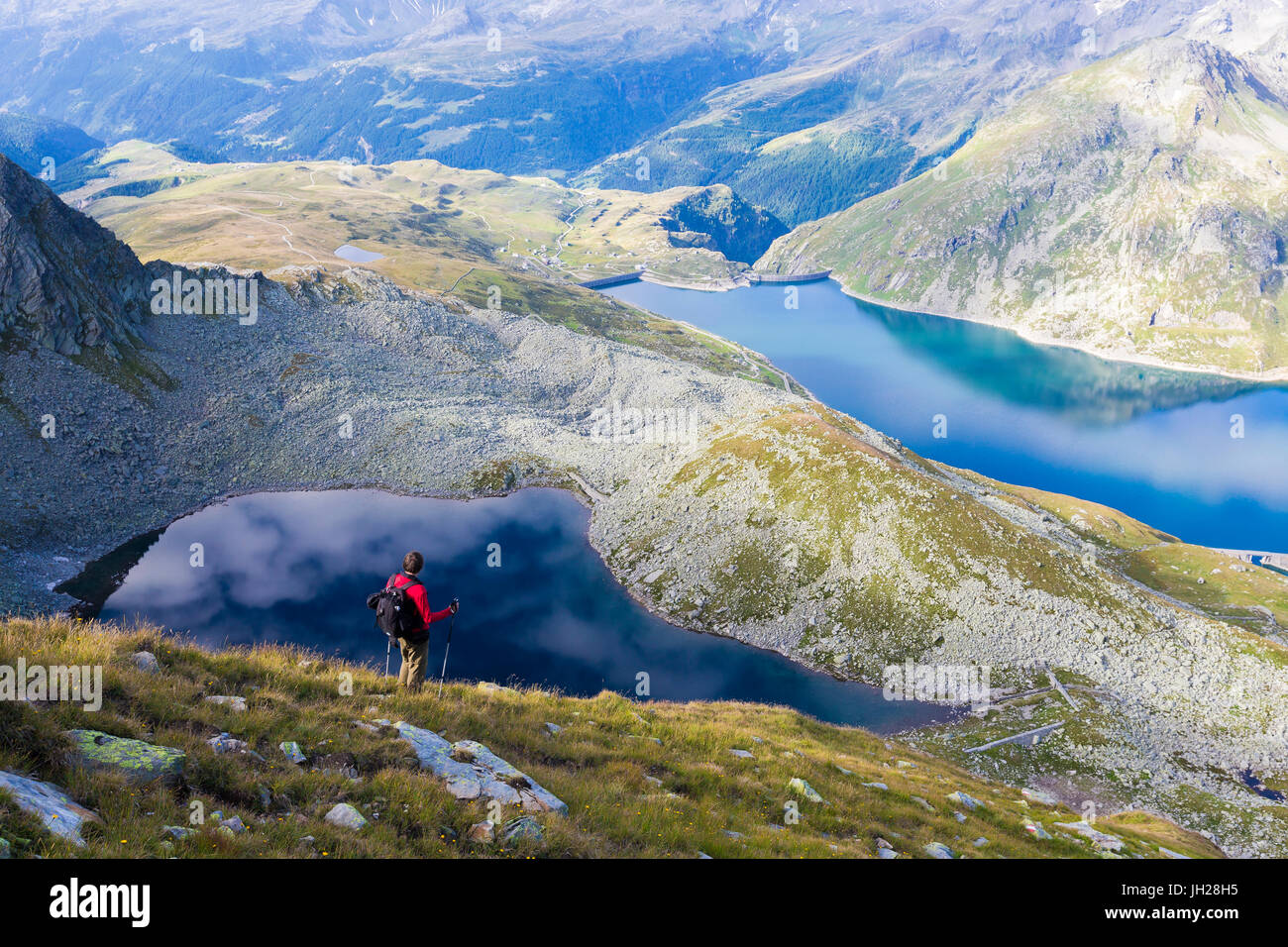 Hiker on the shore of Lago Nero admires the blue Lake Montespluga in summer, Chiavenna Valley, Valtellina, Lombardy, Italy Stock Photo
