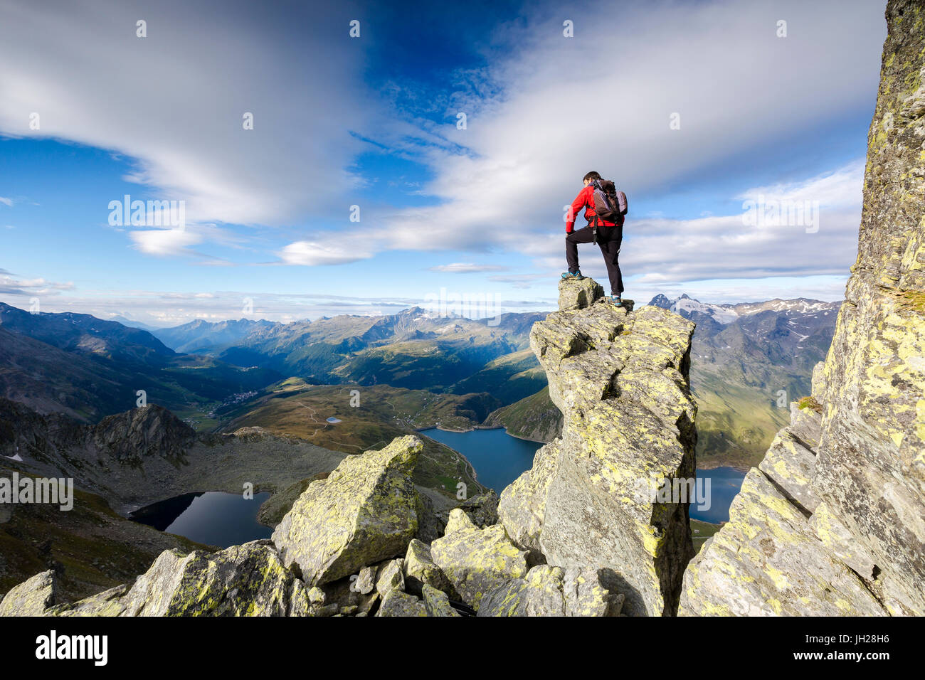 Hiker on top of rocks admires the blue Lake Montespluga in summer, Chiavenna Valley, Valtellina, Lombardy, Italy, Europe Stock Photo