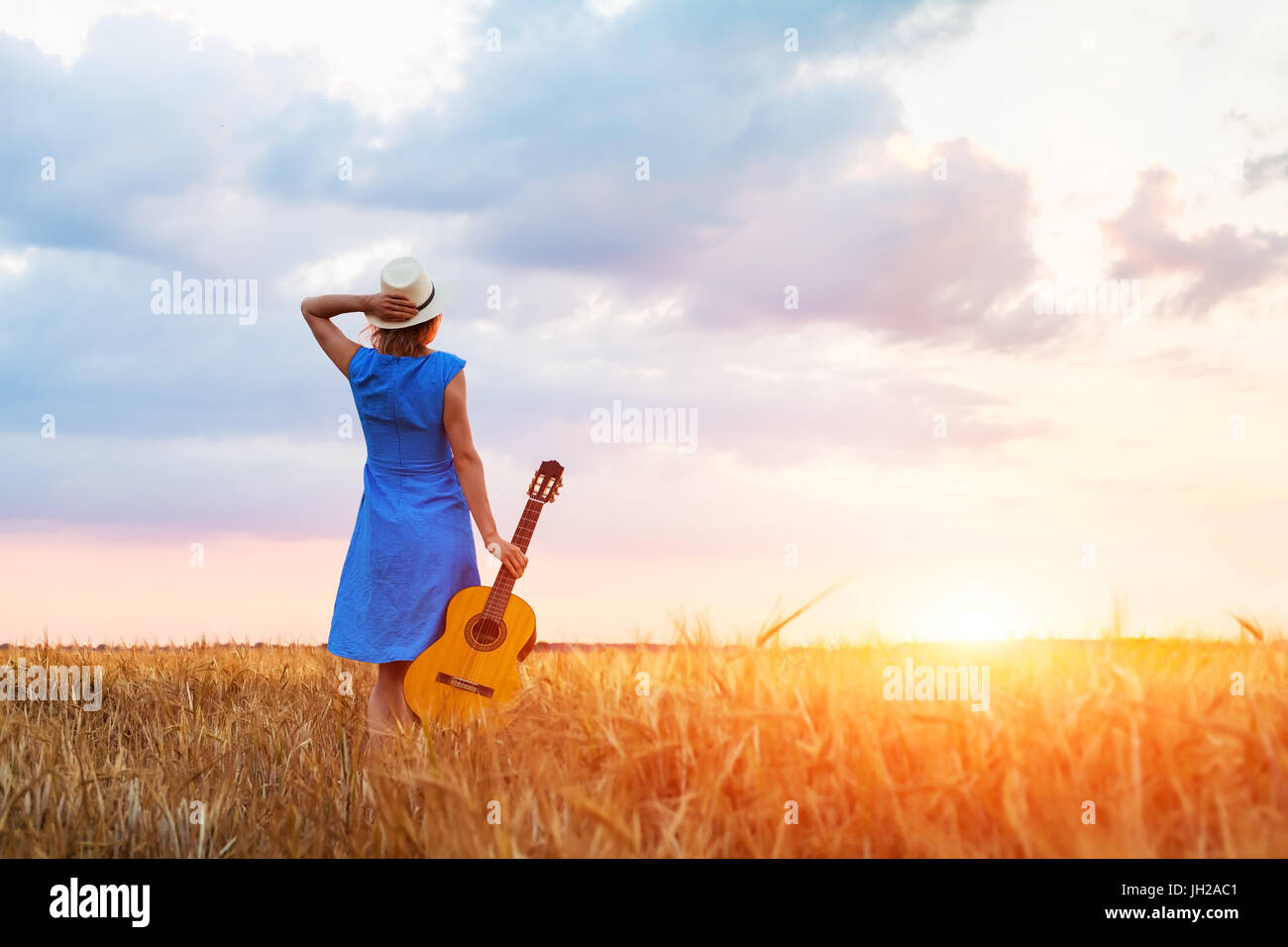 Woman musician with her guitar in the fields looking at sunset, warm summer outdoors Stock Photo