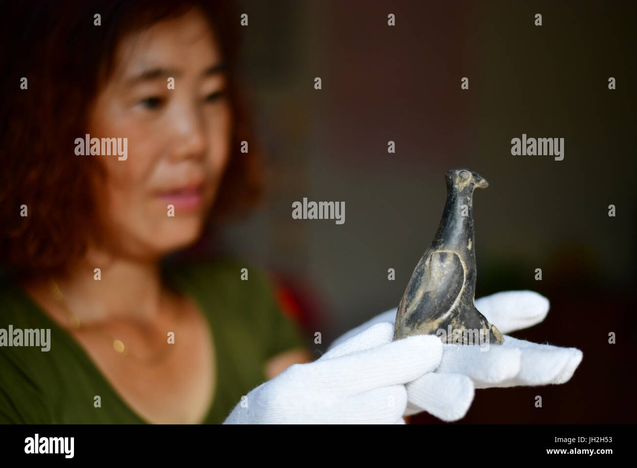 (170712) -- ZHENGZHOU, July 12, 2017 (Xinhua) -- A staff member of Chinese Academy of Social Sciences shows a pottery bird statue in Xinmi, central China's Henan Province, July 10, 2017. Carbon dating has recently confirmed the age of the 3,800-year-old red pottery bird statue, unearthed at the ruins of the city of Xinzhai in Henan Province. The ruins was discovered in 1979 and believed to be founded by Qi, king during the Xia Dynasty, as early as 2050 BC. The statue, 16 cm long and 7 cm tall, was painted red with cinnabar, which suggests it may have been an item of worship, according to arche Stock Photo