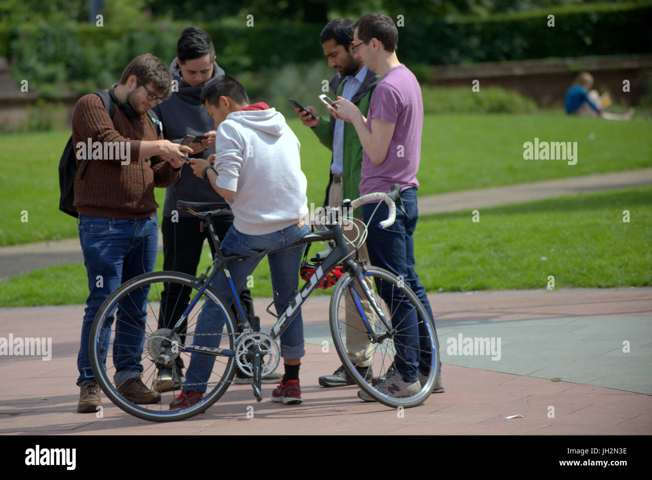 bunch of guys texting smartphones with a bike  together in the centre of Glasgow on a sunny day girl in background Stock Photo