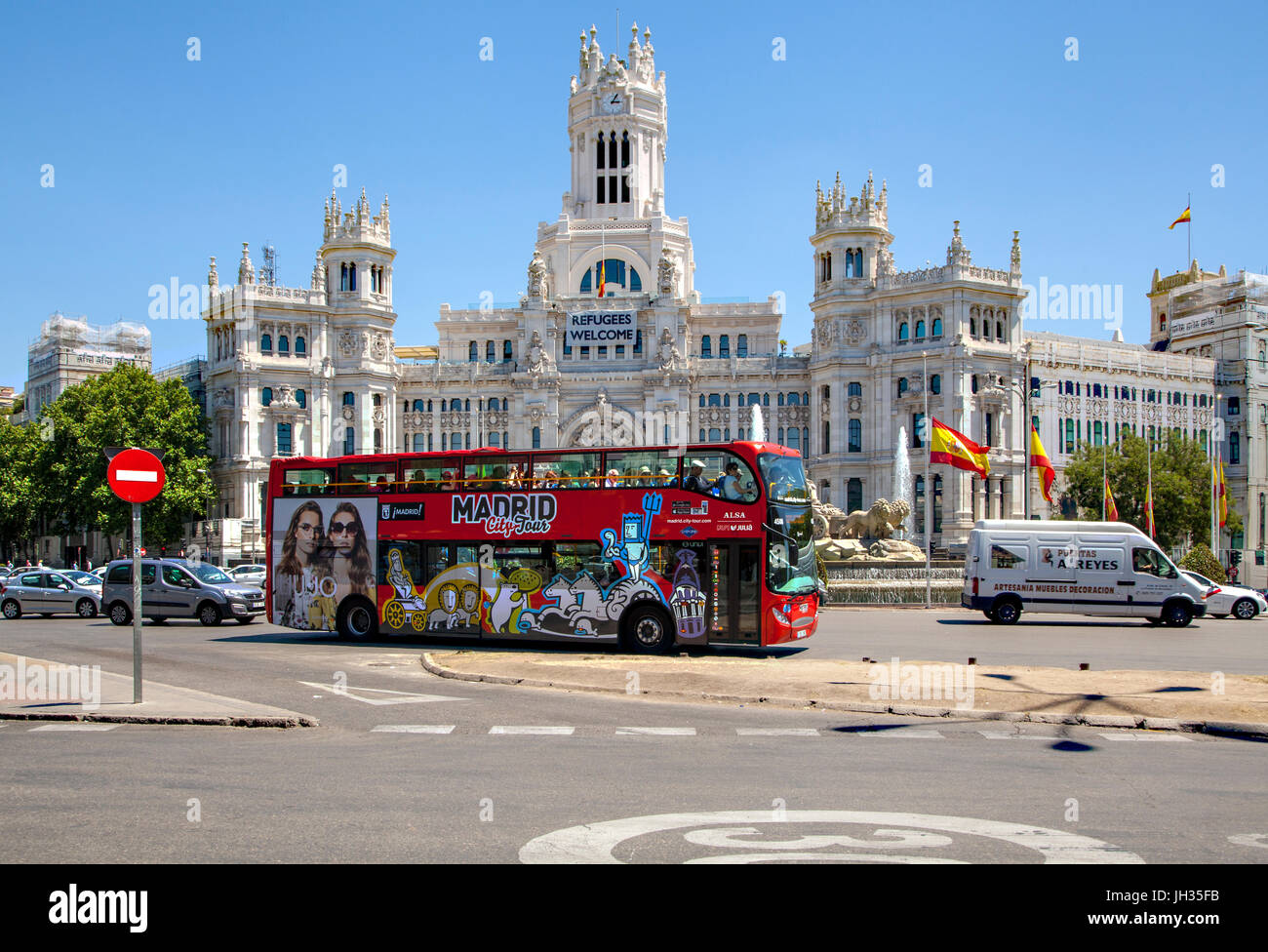 Madrid sightseeing bus driving around the Plaza de Cibeles and passing the Cybele Palace / city hall with a sign saying refugees welcome Stock Photo