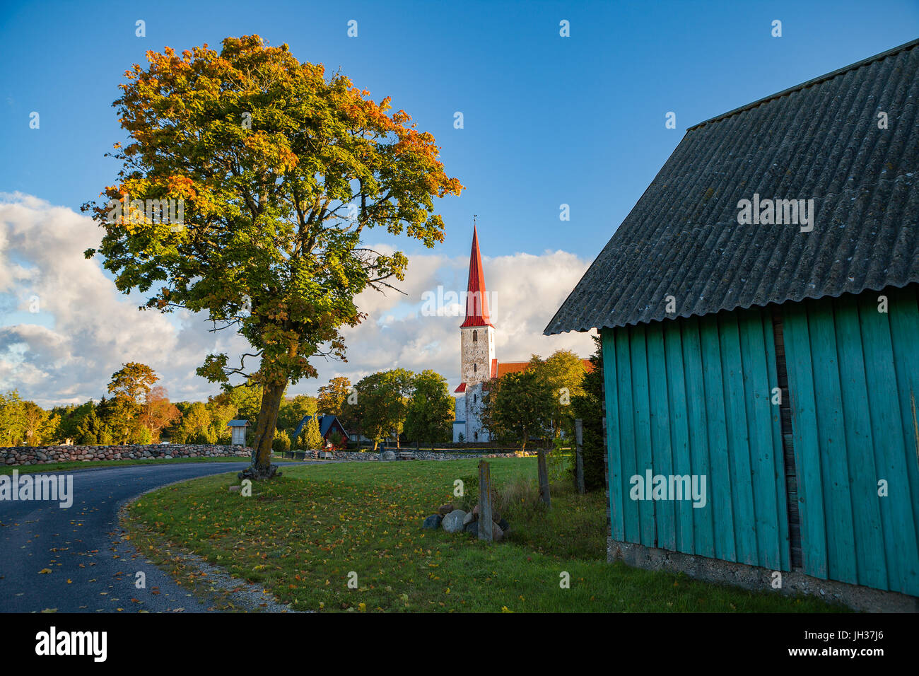 Bellfry and ancient Lutheran church in Kihelkonna, Saaremaa, Estonia. Early autumn sunny day. Village view with road, tree and barn Stock Photo