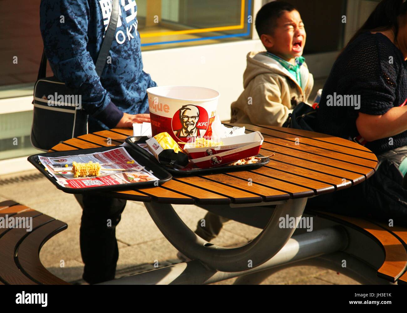 A young Chinese tourist cries as he sits with his parents at the table of a Kentucky Fried Chicken restaurant near the Kaiser Wilhelm Memorial Church in Berlin on October 04, 2017. This picture is part of a series of photos on tourism in Berlin. Photo: Wol | usage worldwide Stock Photo
