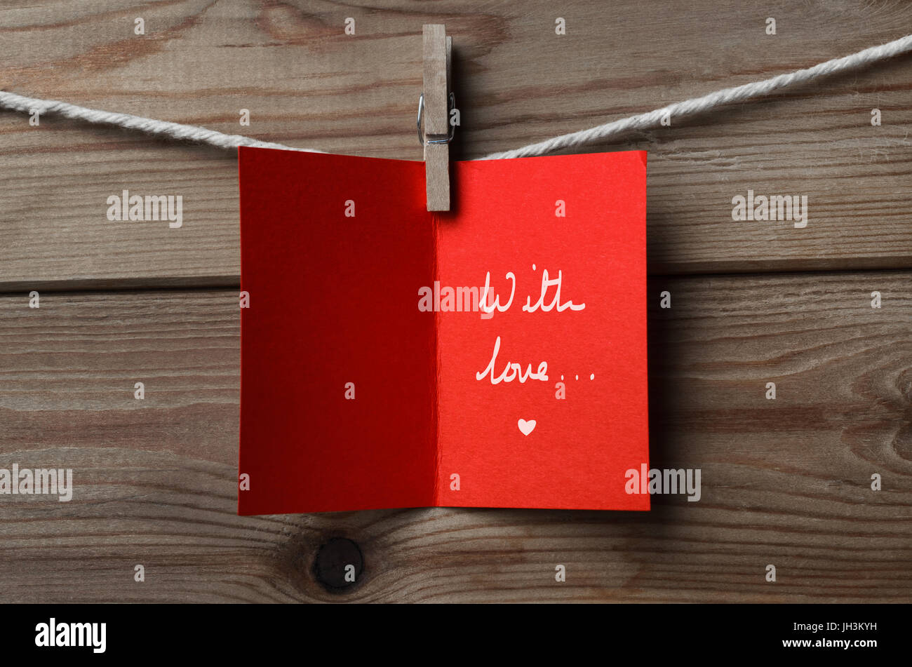 A red greeting card, pegged on to string against wood plank background   Opened to display handwritten words 'With love...' Stock Photo