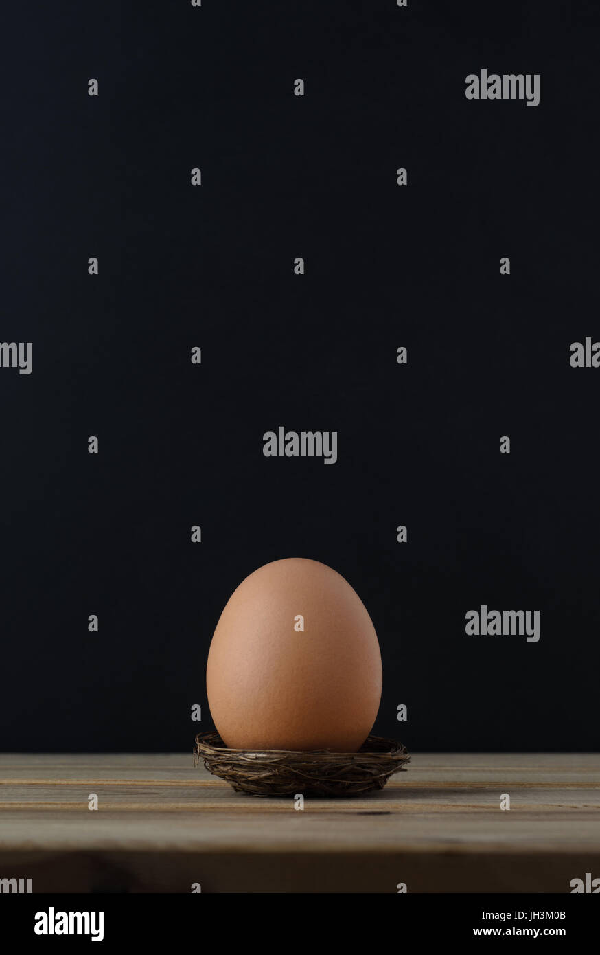 A brown chicken egg in a small nest on wooden plank table with black chalkboard background providing copy space above. Stock Photo