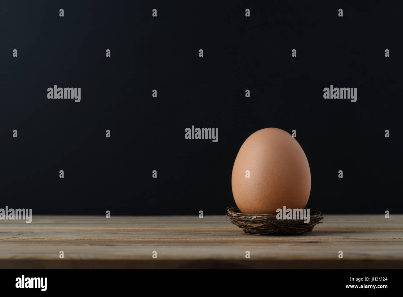 A brown chicken egg in a small nest on wooden plank table with black ...