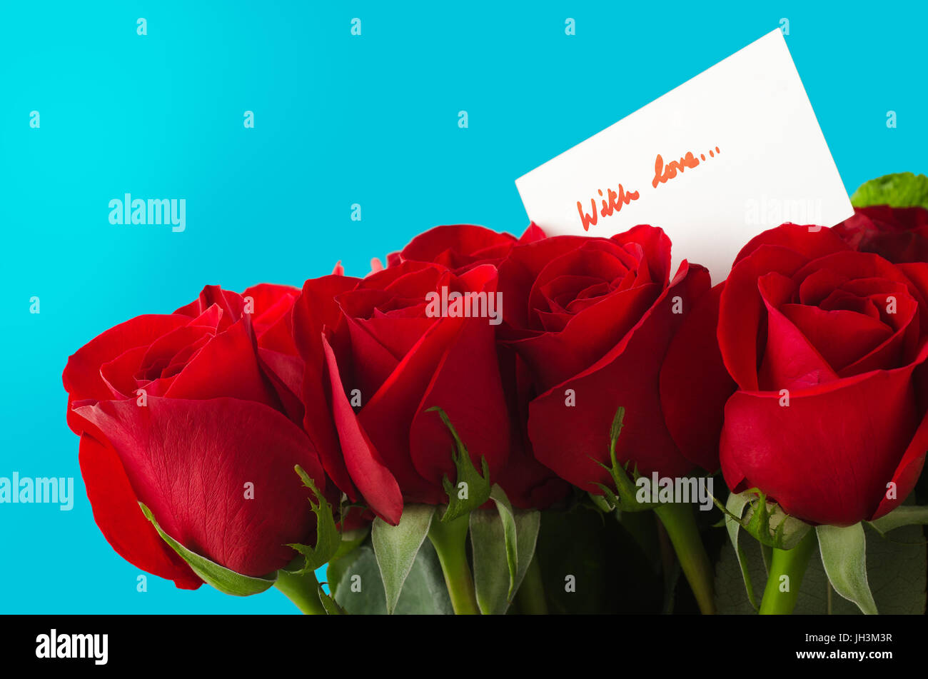 A bouquet of red roses against sky blue background.  A white message card shows 'With Love' in red handwriting. Stock Photo