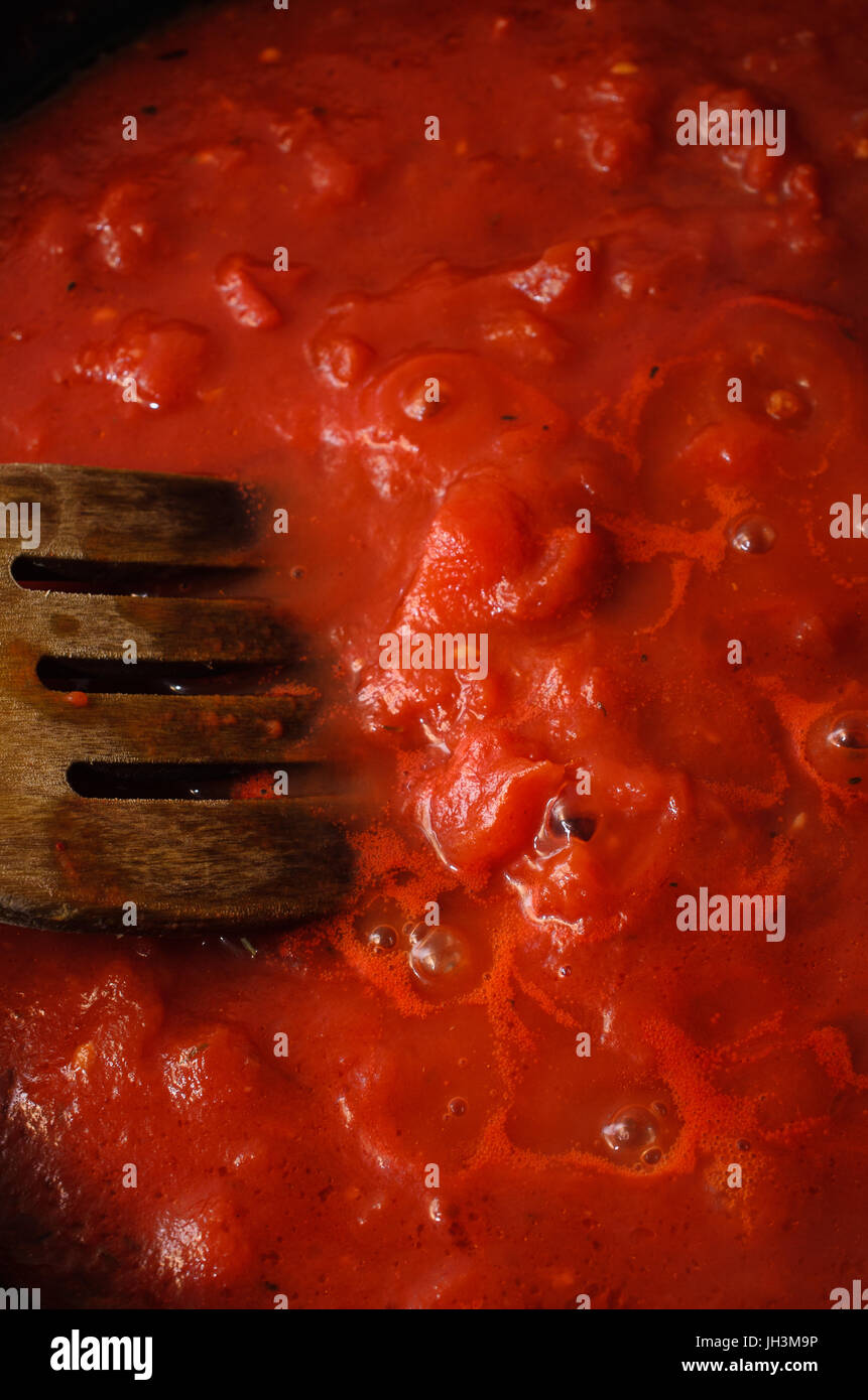 Overhead shot of bubbling hot tomato sauce for pasta, cooking in pan with wooden spatula. Stock Photo