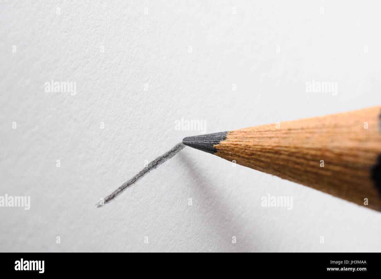 Angled close up (macro) of a graphite pencil drawing a line on textured white paper. Stock Photo