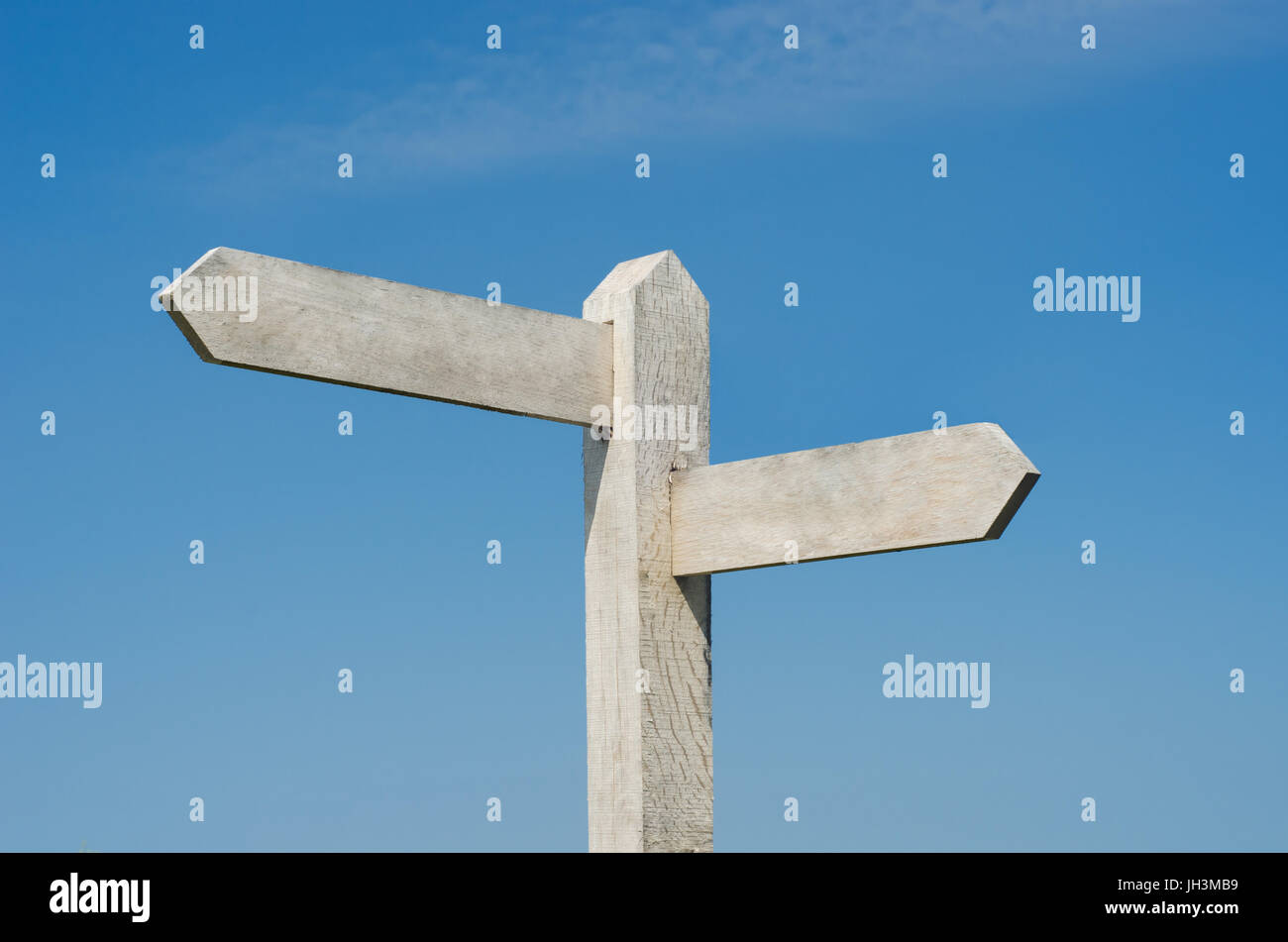 Old wooden signpost with two blank boards pointing  in different directions, weathered to white against bright blue sky with light fluffy clouds. Stock Photo