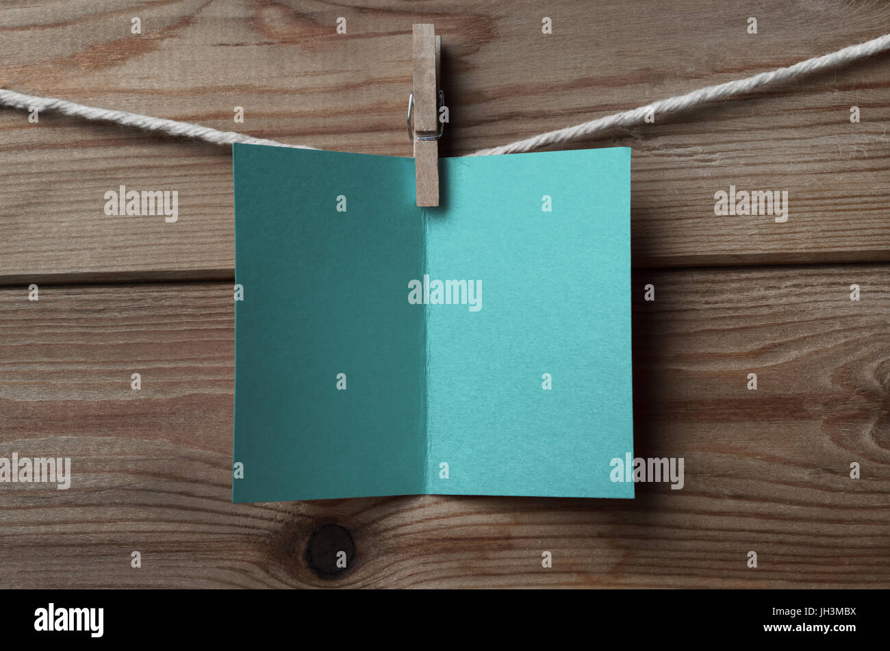 An opened, blank turquoise blue  greeting or Christmas card, pegged on to string against wood plank background Stock Photo