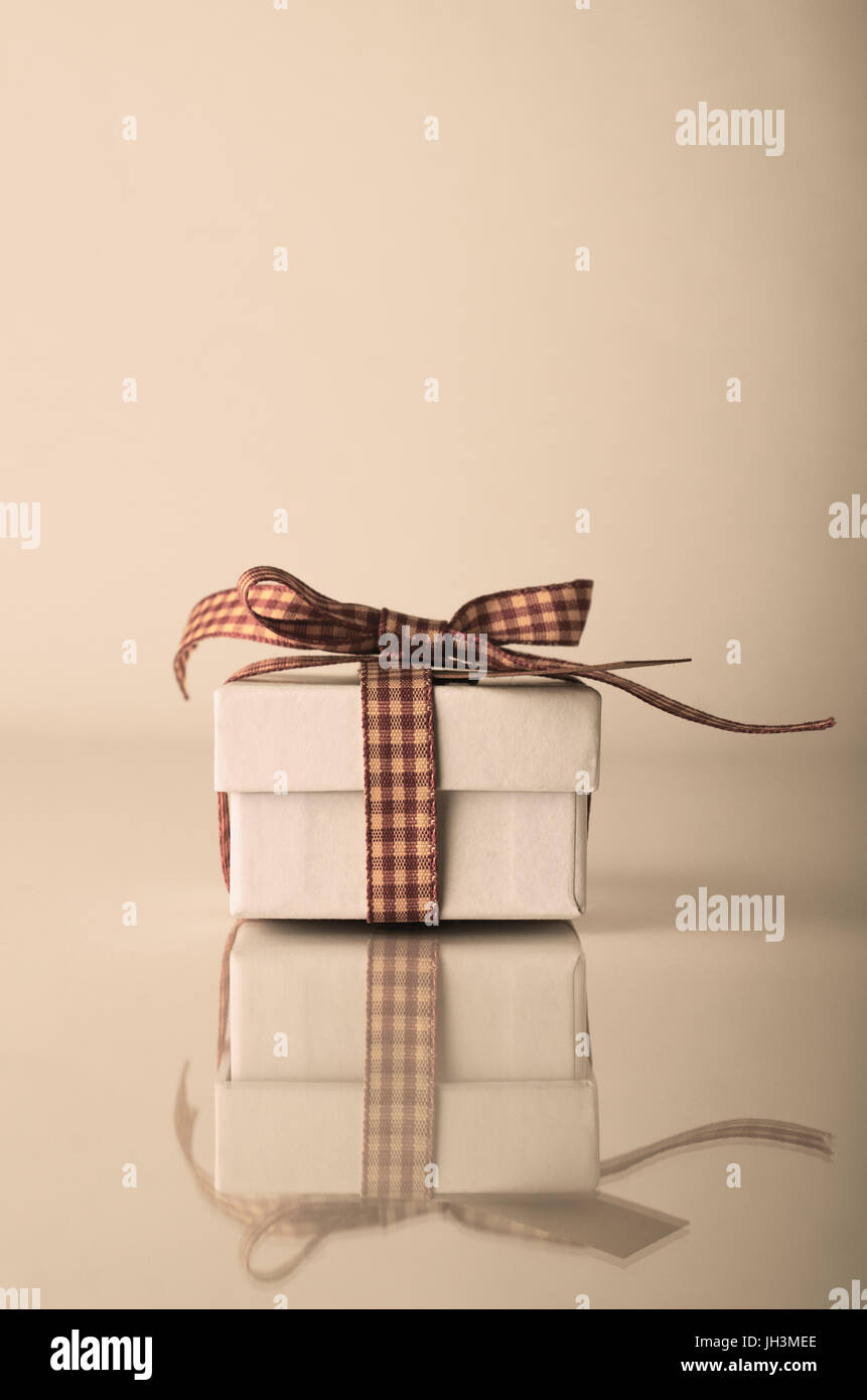 A white, lidded Christmas gift box with gingham ribbon on reflective surface at eye level.   Hues adjusted for retro or vintage effect. Stock Photo