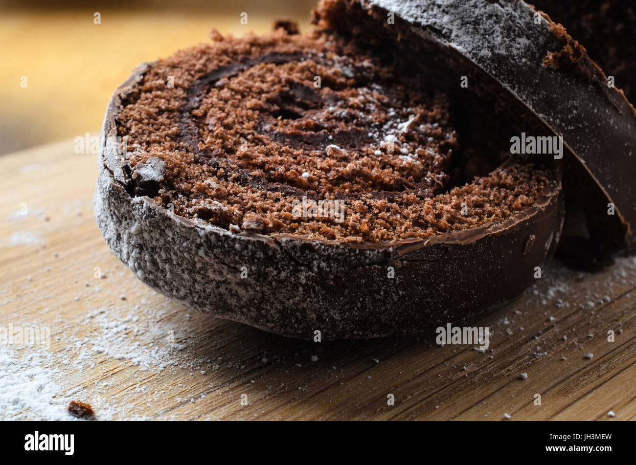 Close up of  sliced chocolate Christmas Yule log, or Swiss Roll cake.  Dusted with icing sugar which has spilled on to wooden chopping board. Stock Photo