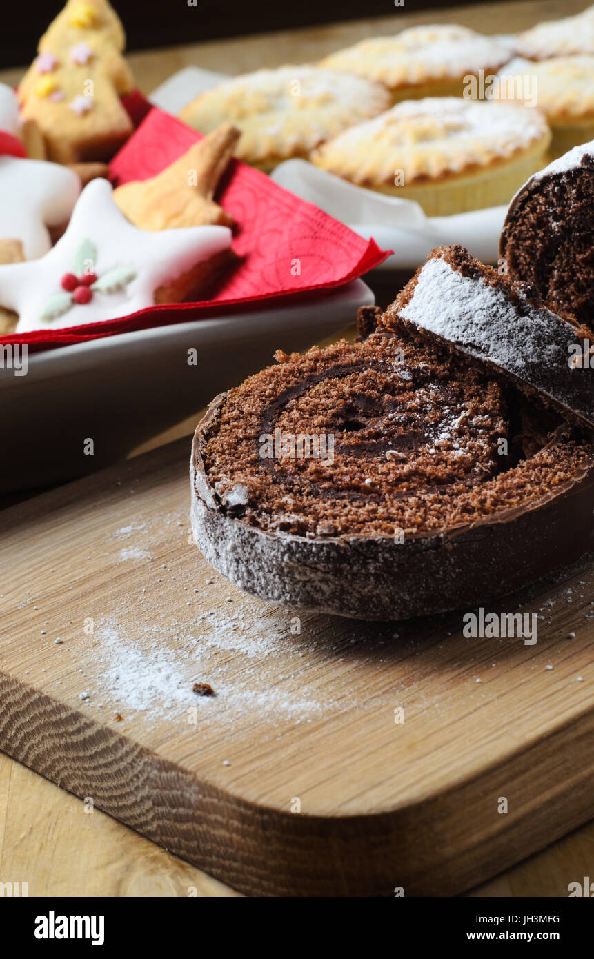 A sweet Christmas dessert buffet on wooden table, with chocolate yule log, shaped biscuits and mince pies in background. Stock Photo