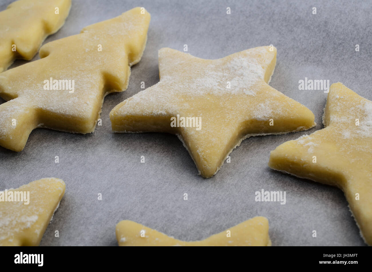 Christmas biscuits or cookie shapes, cut from raw pastry dough on baking parchment paper, ready to go into oven. Stock Photo