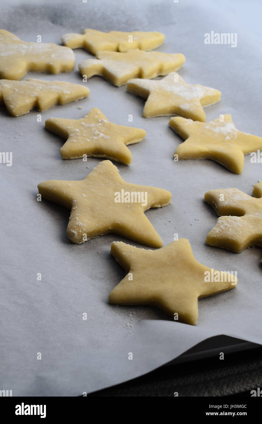 A selection of pastry cut outs from biscuit or cookie dough on a baking tray covered in parchment paper, ready to be baked in oven. Stock Photo