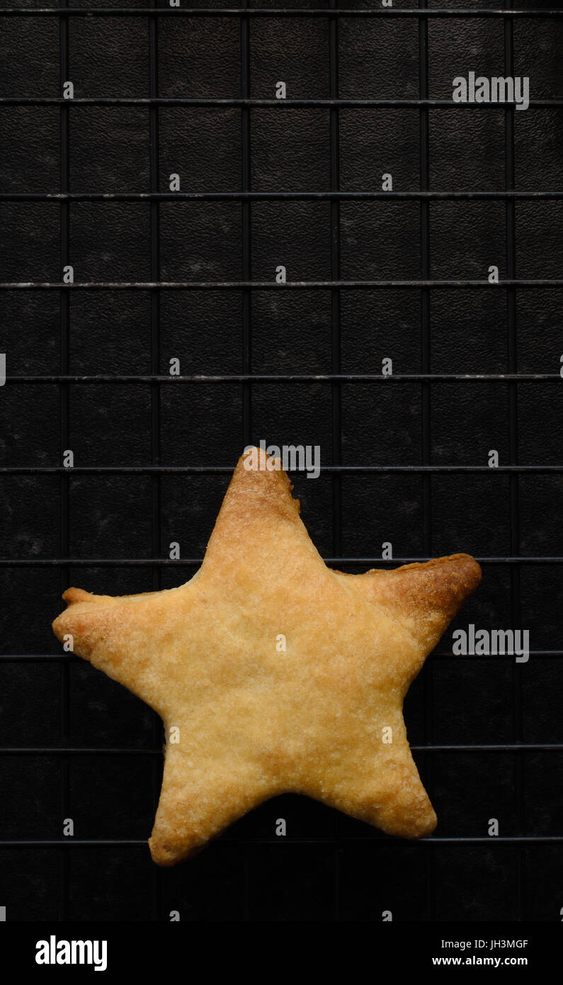 Overhead shot of a single, imperfect star shaped Christmas biscuit, freshly baked and placed on a black wire cooling rack. Stock Photo