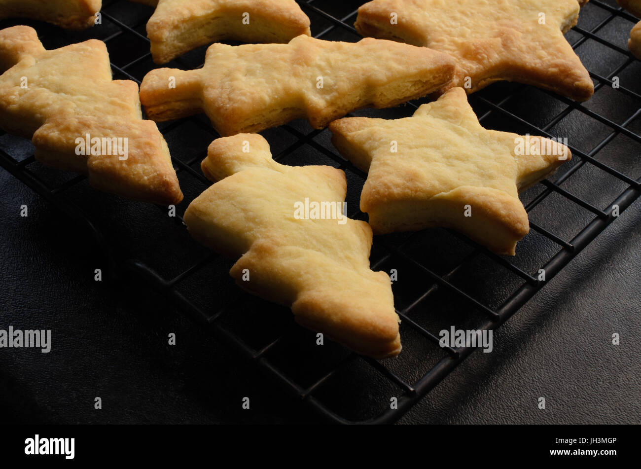 Just baked tree and star shaped Christmas biscuits (cookies), cooling on a black wire rack after removal from oven. Black kitchen worktop below. Stock Photo