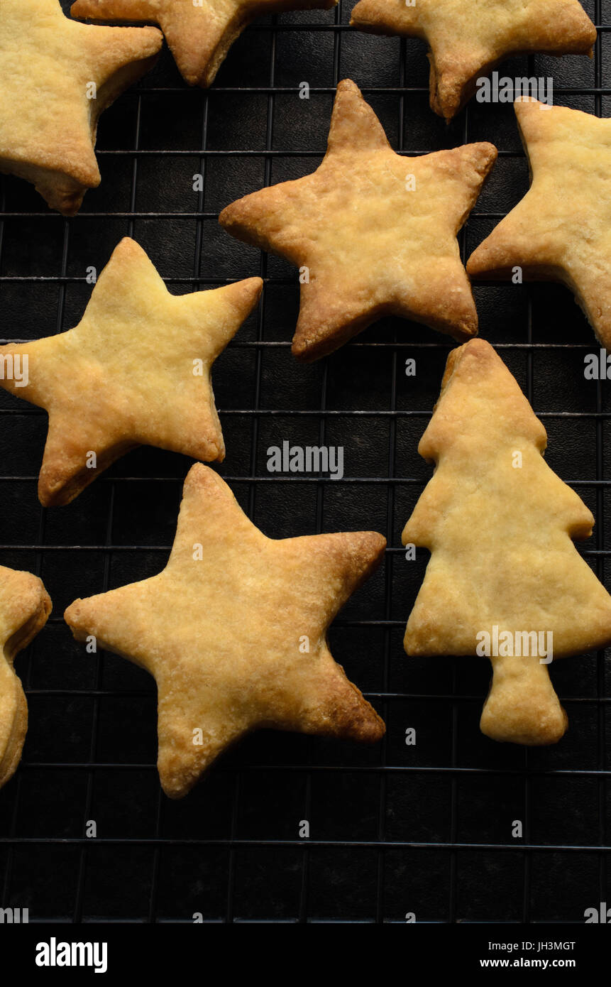 Overhead shot of home baked Christmas biscuits (cookies) selection in tree and star shapes, laid out on black wire cooling rack. Stock Photo