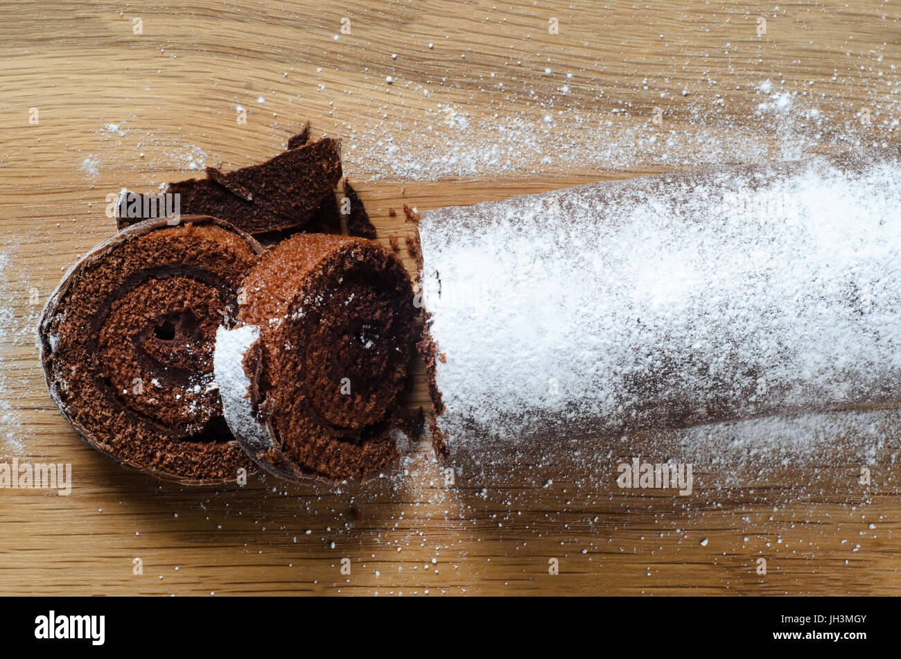 Overhead shot of a chocolate Christmas Yule Log or Swiss Roll cake, sprinkled with icing sugar for snowy appearance on wooden chopping board. Stock Photo