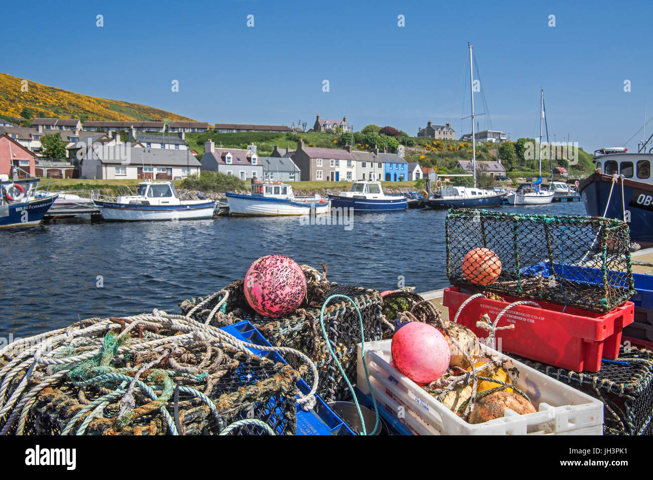 Lobster creels / traps on quay and fishing boats in the harbour of Helmsdale, Sutherland, Scottish Highlands, Scotland, UK Stock Photo