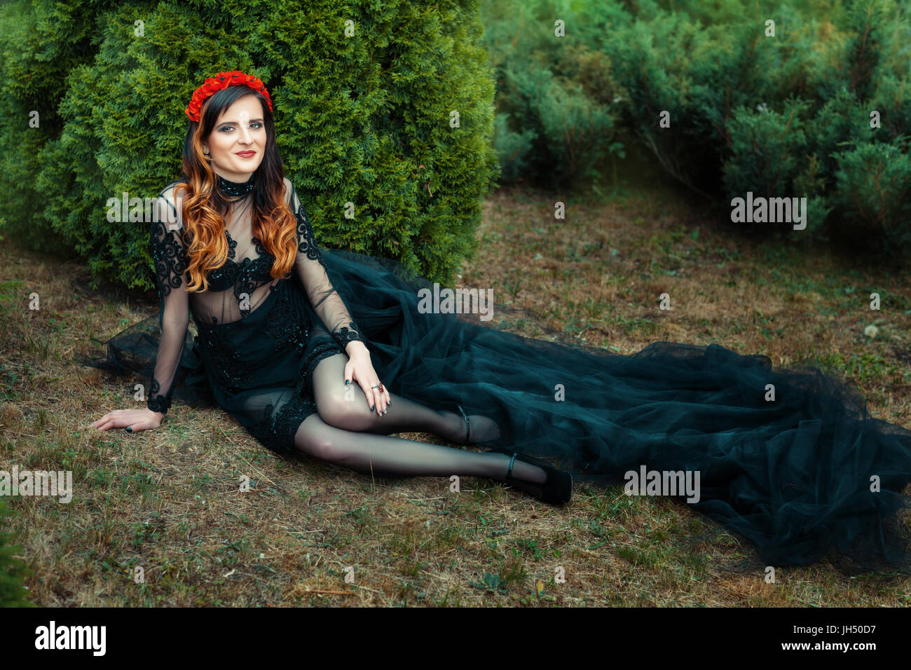 On the grass in a park beautiful girl sitting. Long dress with black ...