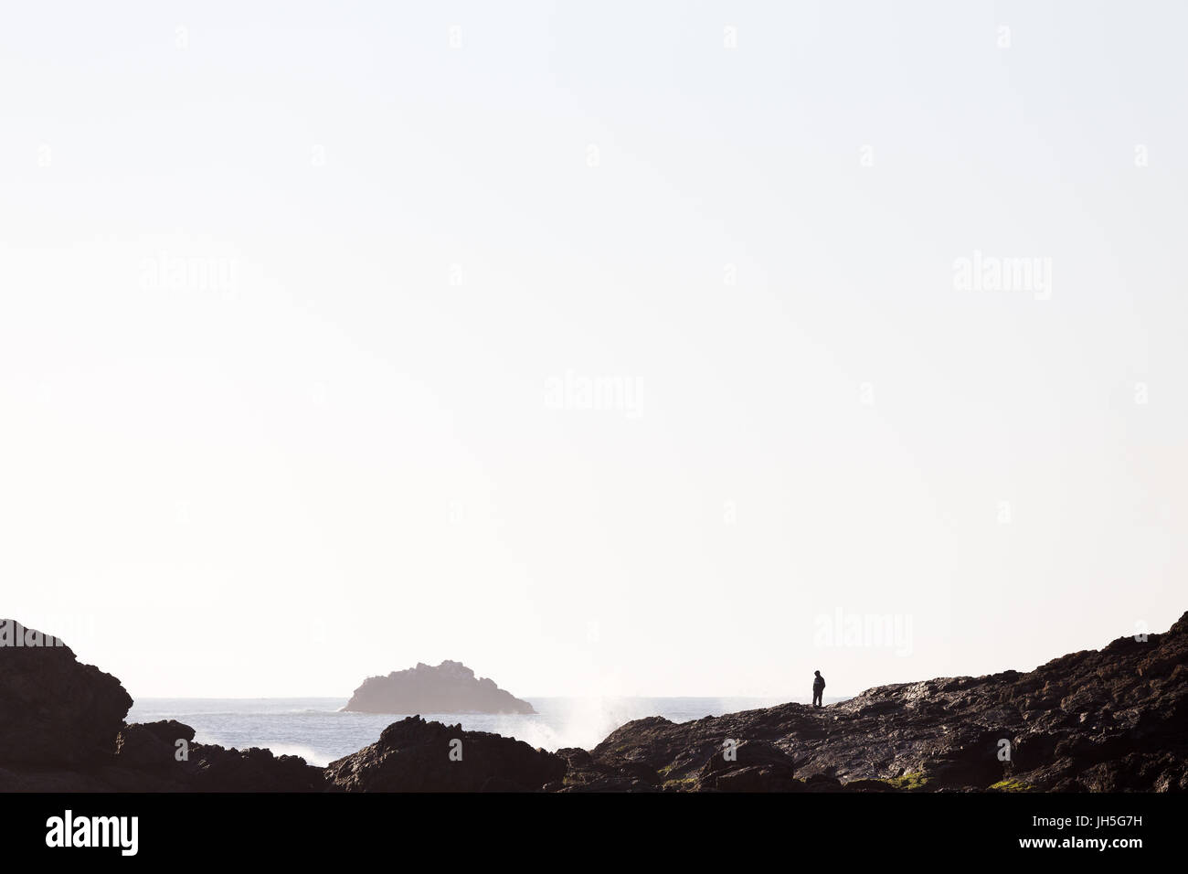A person is silhouetted by bright morning light in a beautiful coastline seascape. Stock Photo