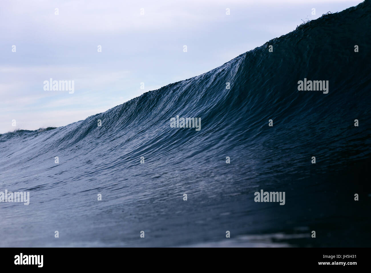 A dark, ominous ocean wave looms on a stormy overcast day. Stock Photo