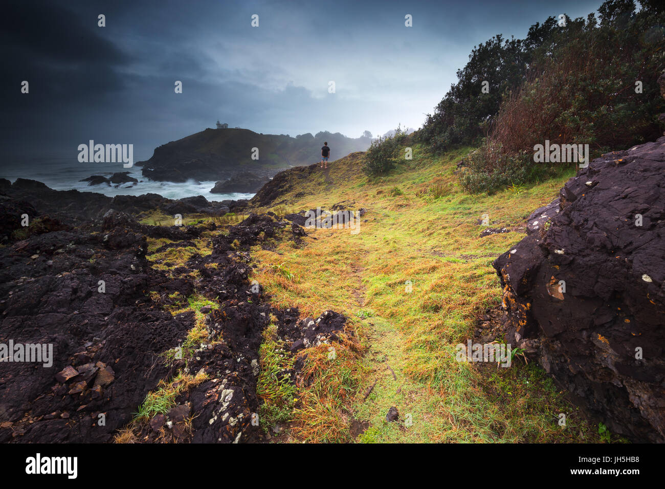 A person looks on as a dark moody storm moves over the rugged coastline that surrounds. Stock Photo