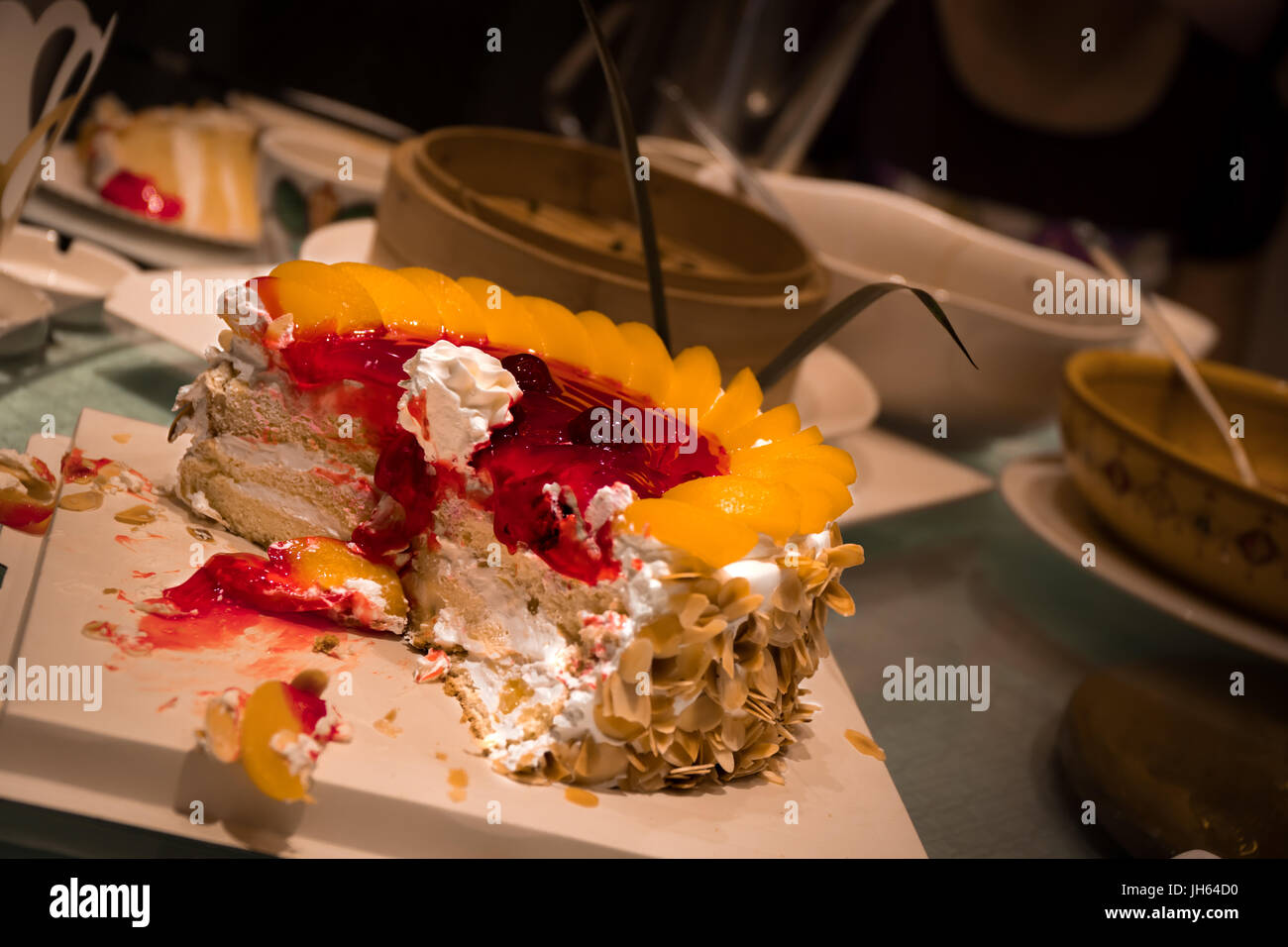 A partly eaten and cut birthday cake sitting on a restaurant table with other dishes in the background. Stock Photo