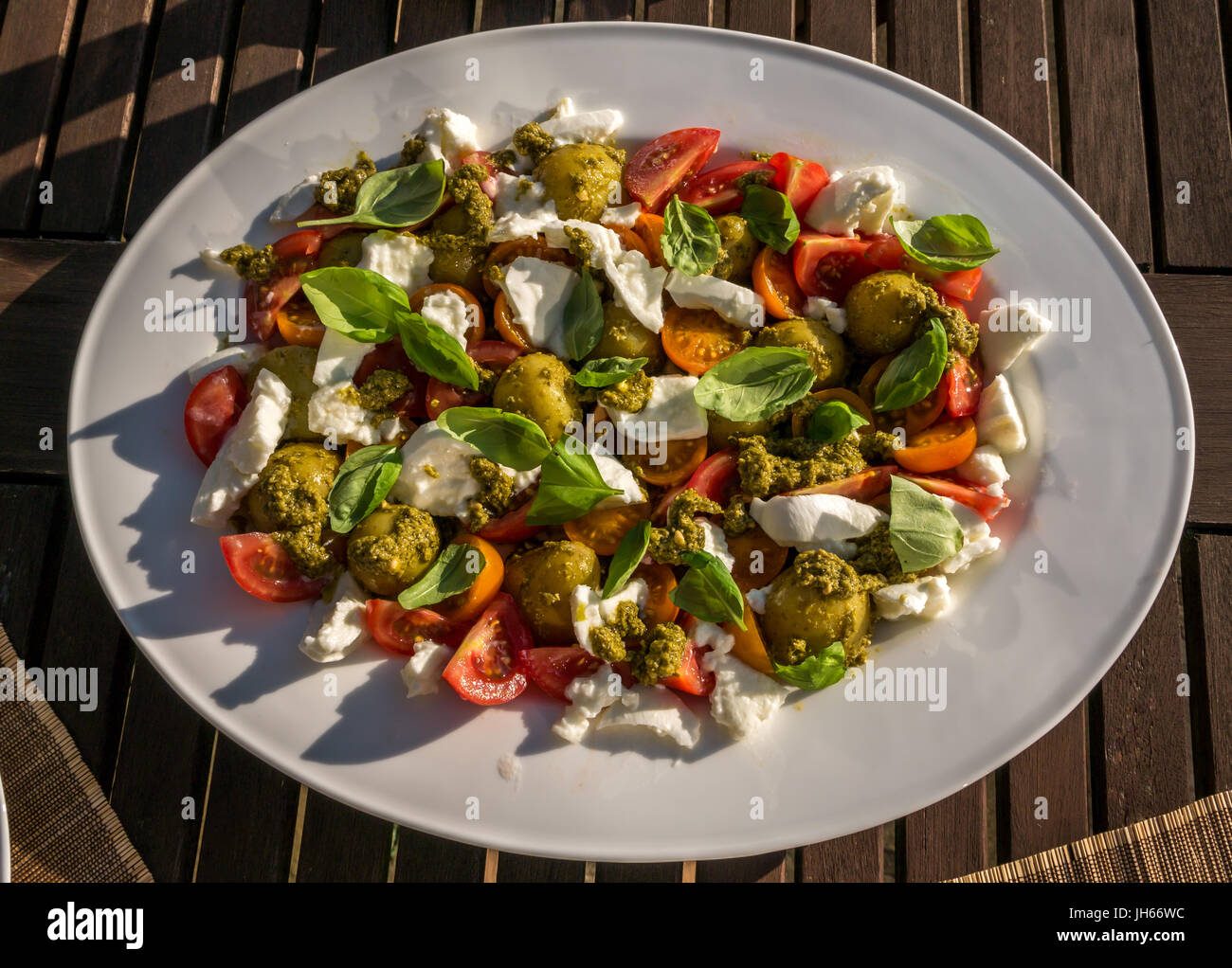 Caprese salad with pesto and cold boiled potatoes, served on white crockery, on garden patio table in Summer sunshine, Scotland, UK Stock Photo