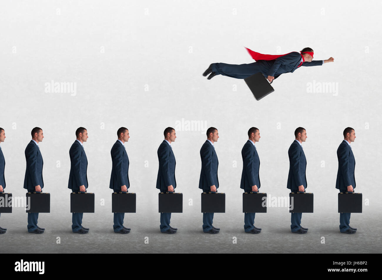 superhero businessman overcoming inertia flying away from a static queue of businessmen Stock Photo