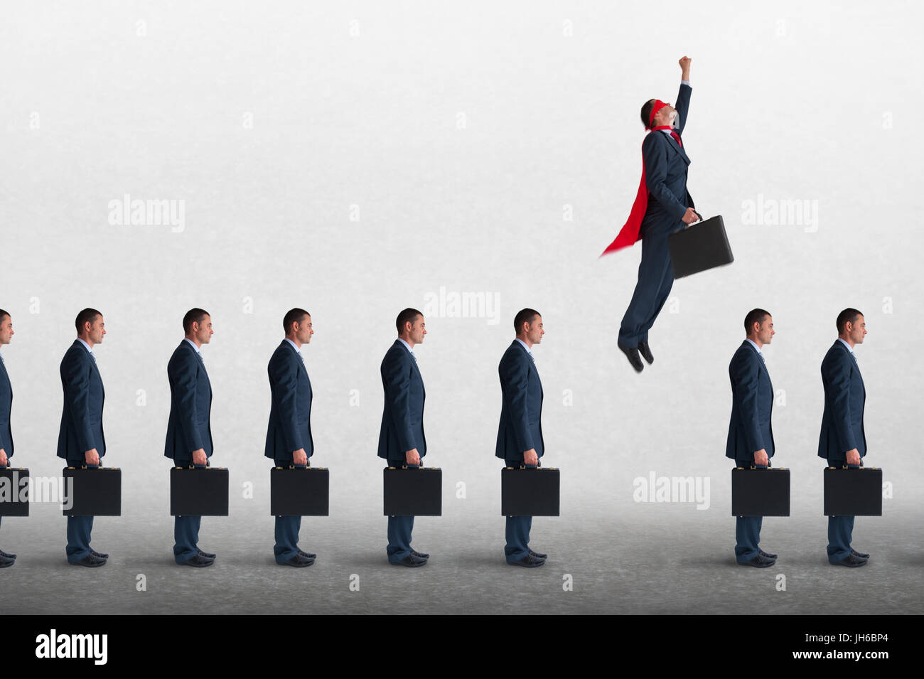 superhero businessman overcoming inertia flying away from a static queue of businessmen Stock Photo